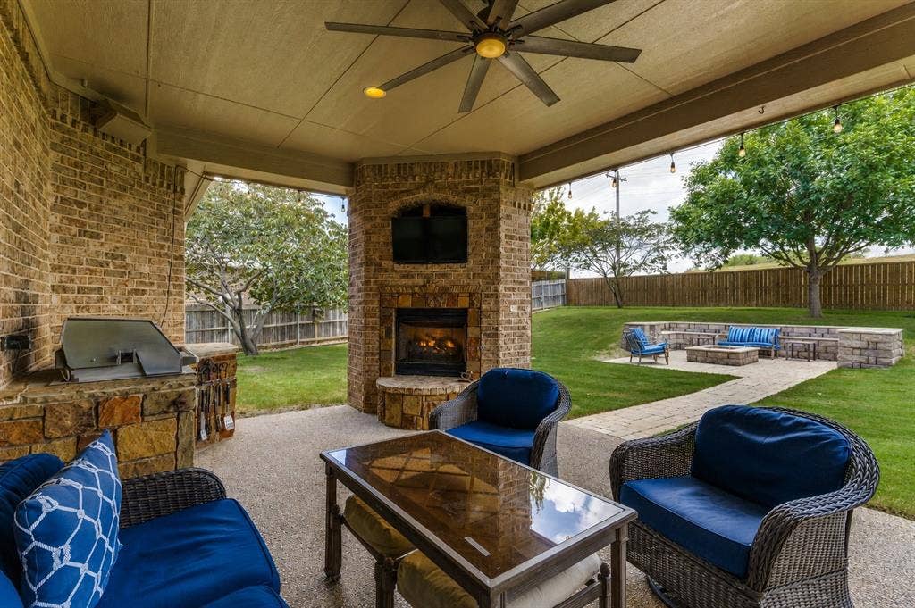 Expansive covered patio featuring a brick and stone outdoor fireplace, a built-in barbecue grill station, and a ceiling fan