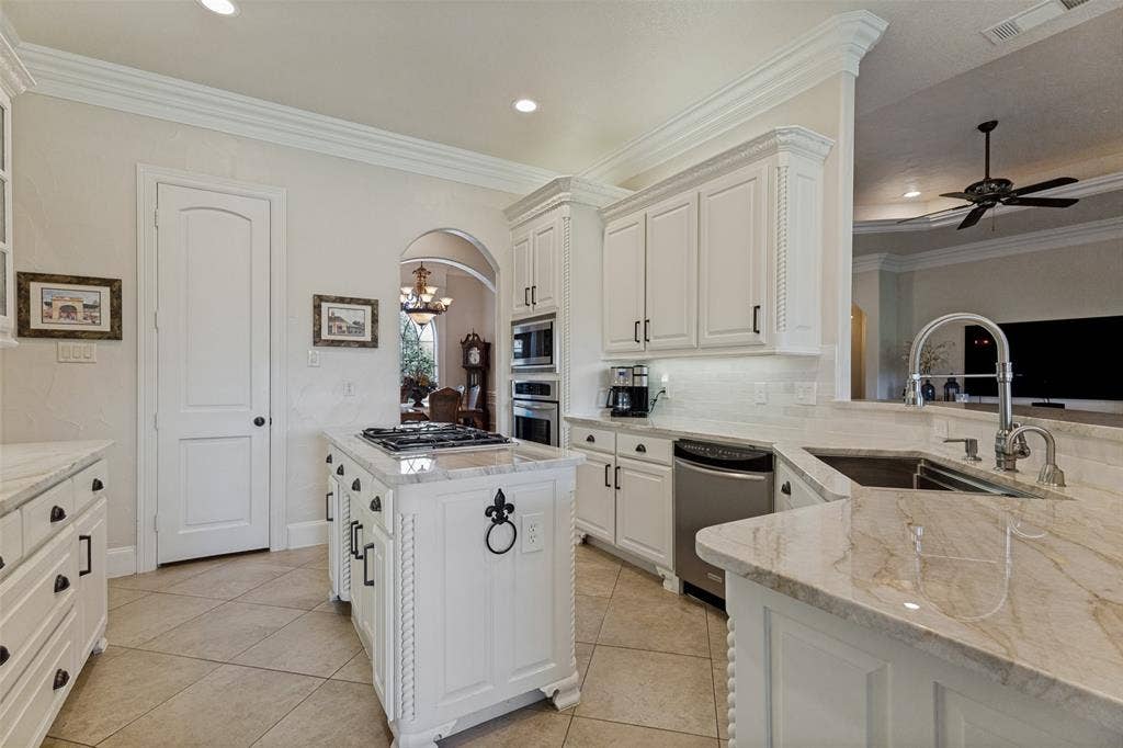 Gourmet kitchen featuring a central island with built-in cooktop, extensive white cabinetry, light-toned stone countertops, and tile flooring