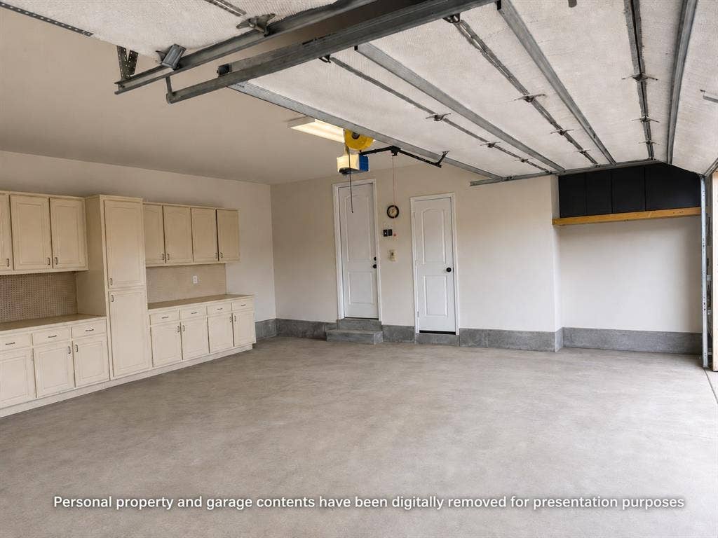 Spacious garage featuring extensive built-in cabinetry, a durable concrete floor, two interior access doors, and overhead lighting