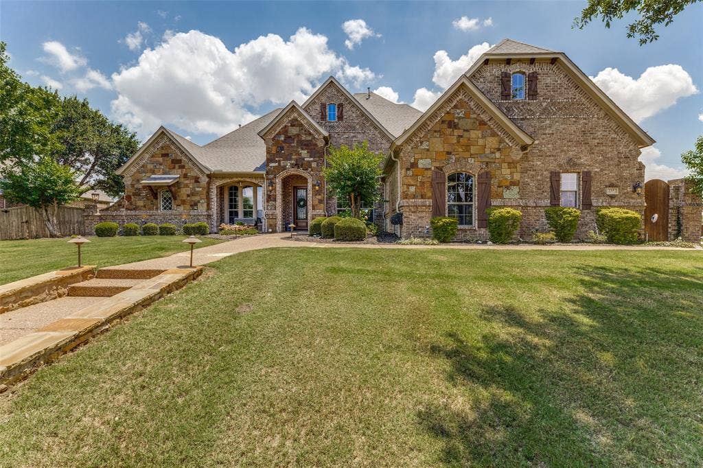 Stone and brick exterior featuring multiple gables, arched entryways, dark wood shutters, a covered porch, and a stone walkway with integrated lighting