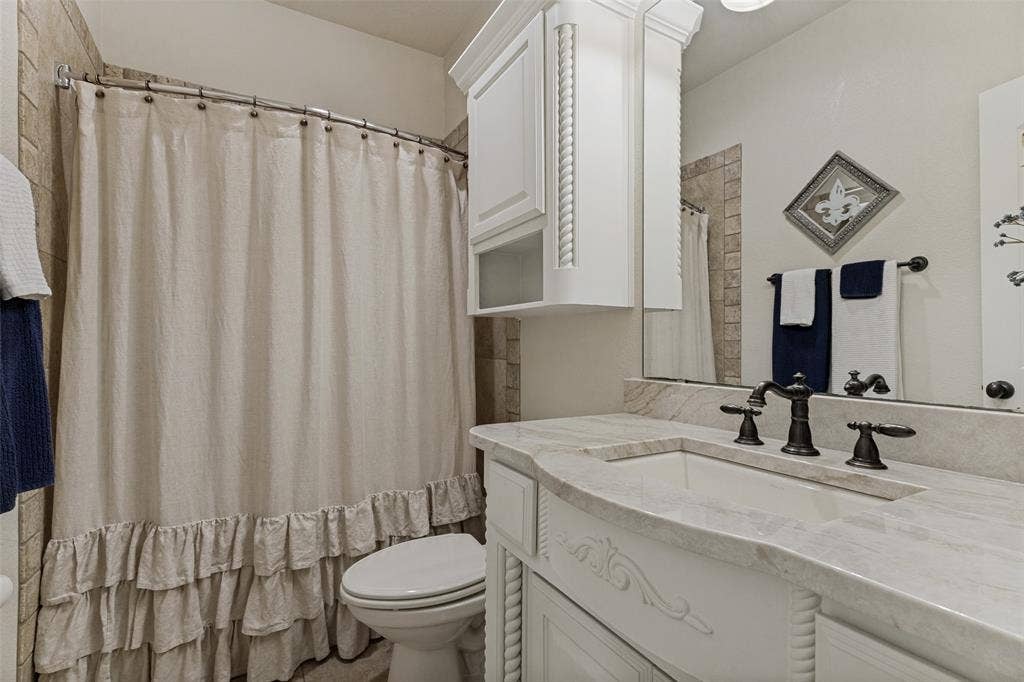 Bathroom featuring a built-in vanity with a light-toned countertop and integrated sink, dark-toned faucet, wall-mounted mirror, and white cabinetry