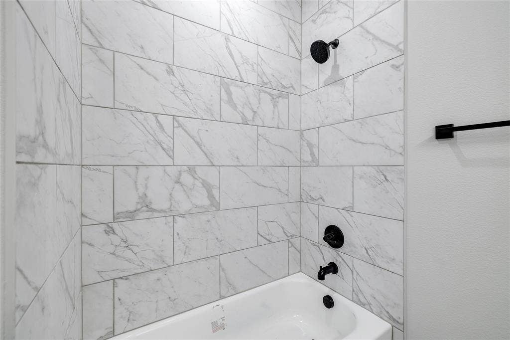 6600-6602 Florence Drive, Midlothian, TX 76065 White subway tile with gray veining surrounds a built-in bathtub with matte black fixtures, including a showerhead, faucet, and drain
