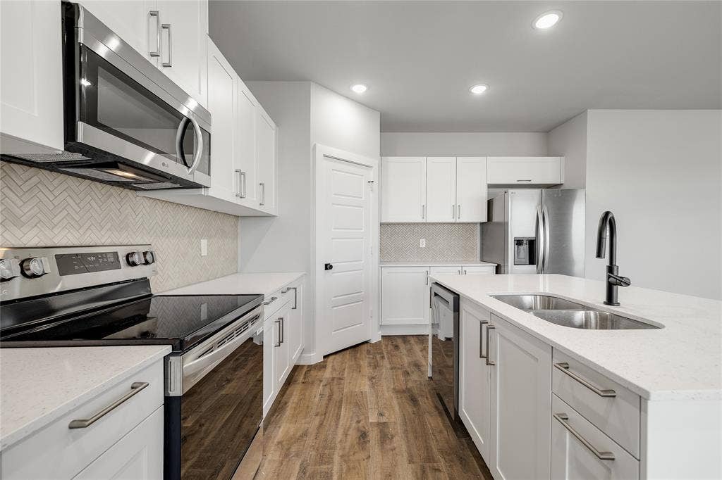6600-6602 Florence Drive, Midlothian, TX 76065 Modern kitchen featuring white cabinetry, light countertops, wood-finish flooring, stainless steel appliances, and a herringbone tile backsplash