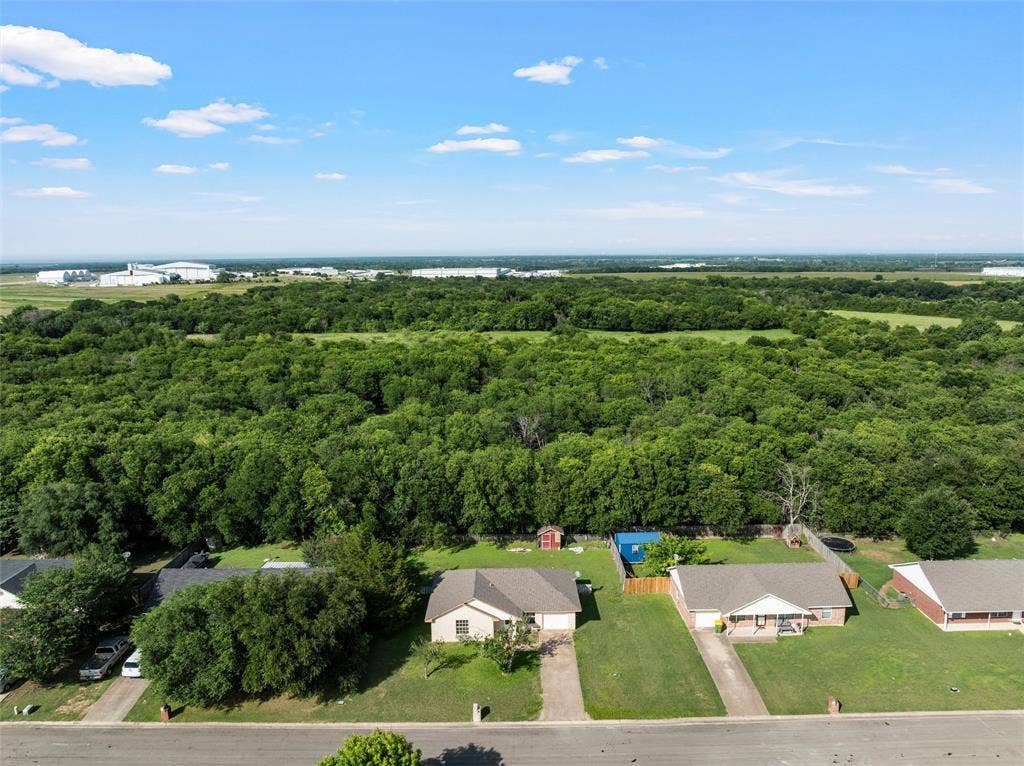 1307 Luanne, Bellmead, TX 76705 Aerial perspective showcasing residential properties bordering a dense wooded area and open fields