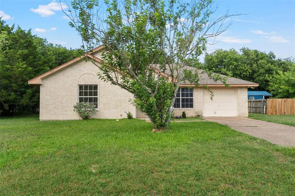 1307 Luanne, Bellmead, TX 76705 Single-story residence featuring light-colored brick veneer, an attached garage, a concrete driveway, a gabled roofline, and established landscaping