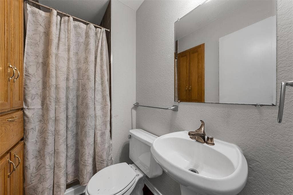 1307 Luanne, Bellmead, TX 76705 Bathroom featuring a pedestal sink with a bronze-finish faucet, wall-mounted mirror, and a shower with a patterned curtain