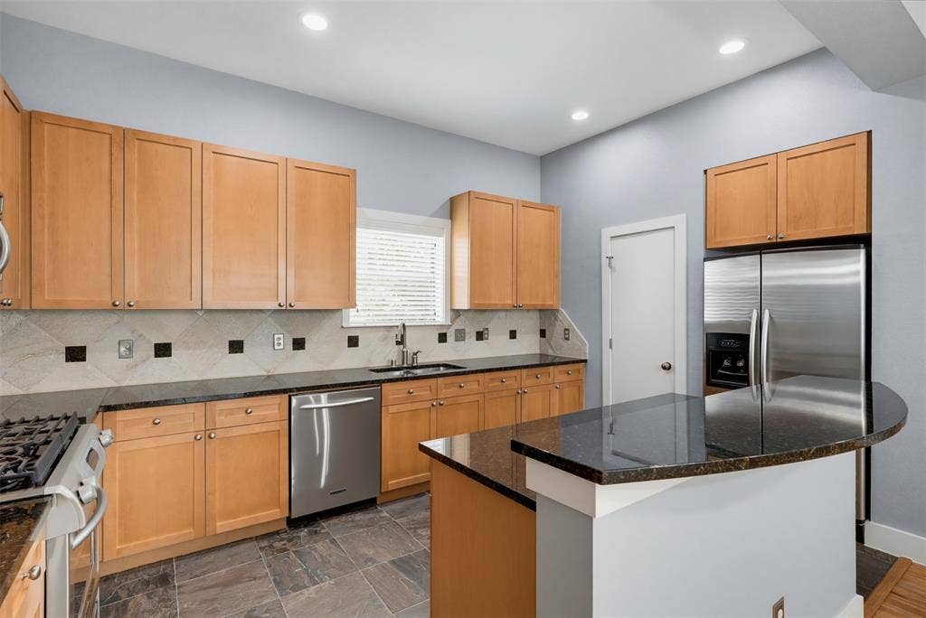 4830 Cedar Springs Road, #30, Dallas, TX 75219 Kitchen featuring light wood cabinetry, granite countertops, stainless steel appliances, a tiled backsplash with accent squares, and slate-finish floor tiles