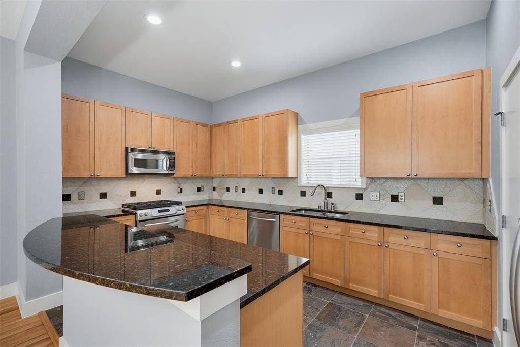 4830 Cedar Springs Road, #30, Dallas, TX 75219 Kitchen featuring a curved peninsula with a dark countertop, light wood cabinetry, a stainless steel microwave, a stainless steel range, and a stainless steel dishwasher