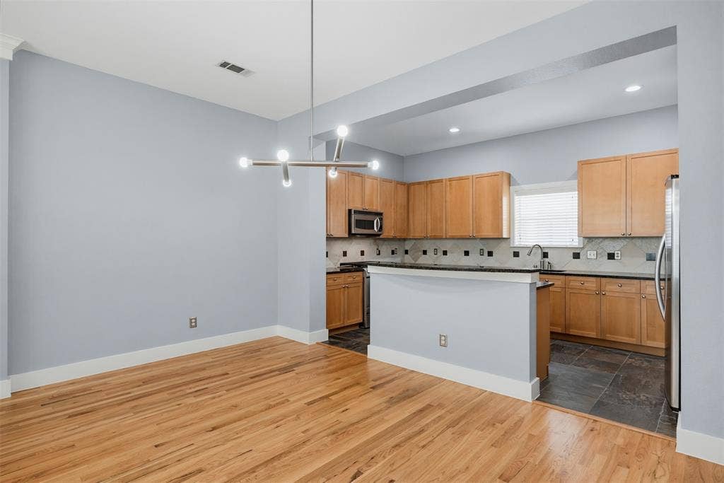 4830 Cedar Springs Road, #30, Dallas, TX 75219 Open-concept living area featuring wood-finish flooring, a contemporary linear chandelier, and a kitchen with wood cabinetry, stainless steel appliances, and a tiled backsplash