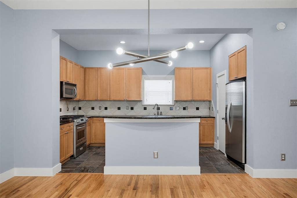 4830 Cedar Springs Road, #30, Dallas, TX 75219 Kitchen with natural wood cabinetry, stainless steel appliances, dark countertops, and a tiled backsplash