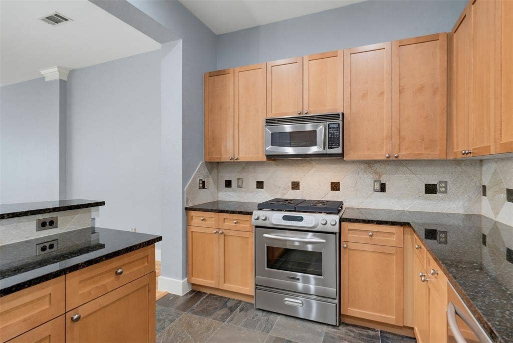 4830 Cedar Springs Road, #30, Dallas, TX 75219 Kitchen featuring wood-finish cabinetry, black stone countertops, stainless steel appliances, and a decorative tile backsplash