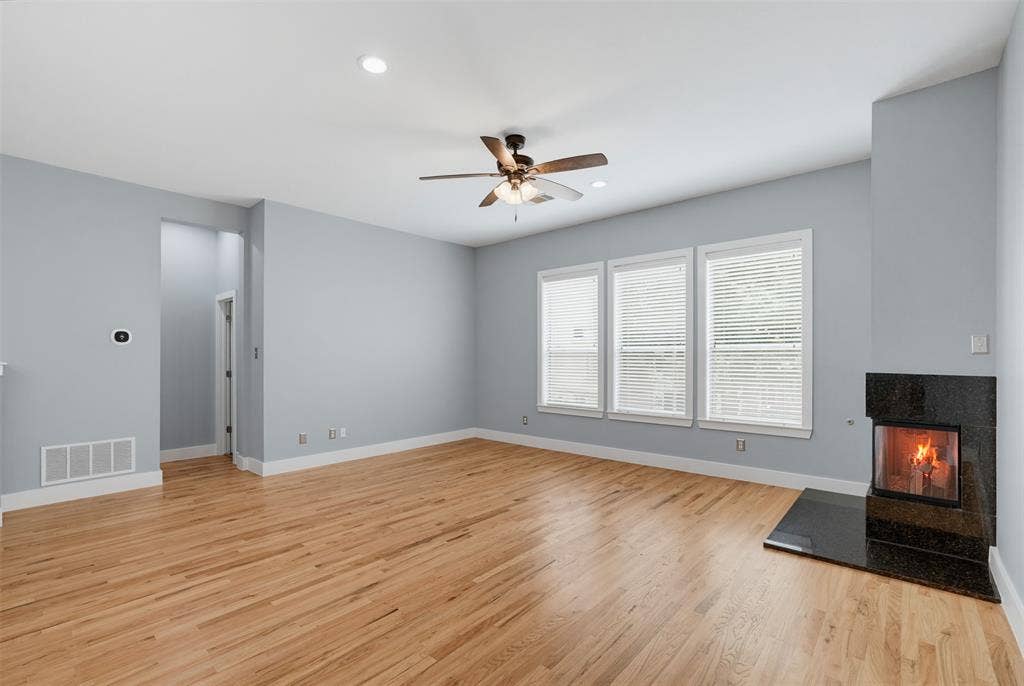 4830 Cedar Springs Road, #30, Dallas, TX 75219 Spacious room featuring wood-finish flooring, a contemporary fireplace with a dark stone surround and hearth, and three large windows