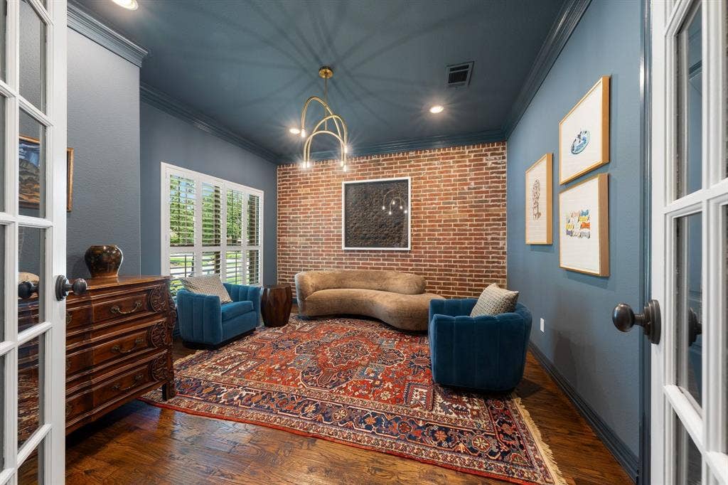 Color drenched sitting room with brick accent wall and modern chandelier.