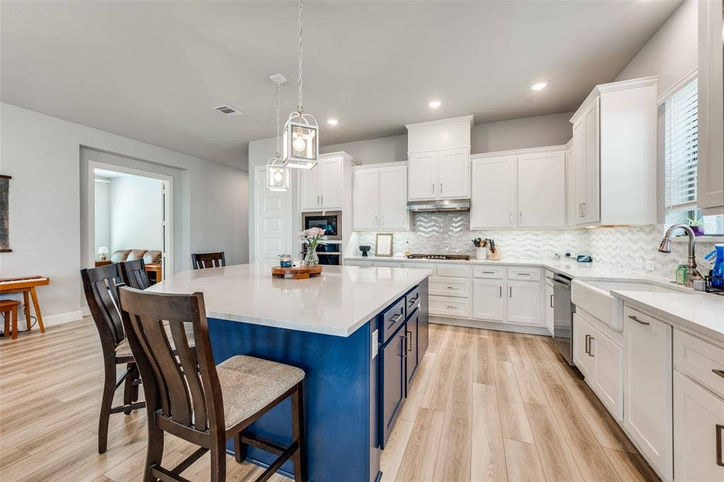 2703 Trinity Ridge Street, Mansfield, TX 76063 Kitchen featuring an expansive center island with seating, white shaker cabinetry, light wood-finish flooring, white countertops, and a white farmhouse sink
