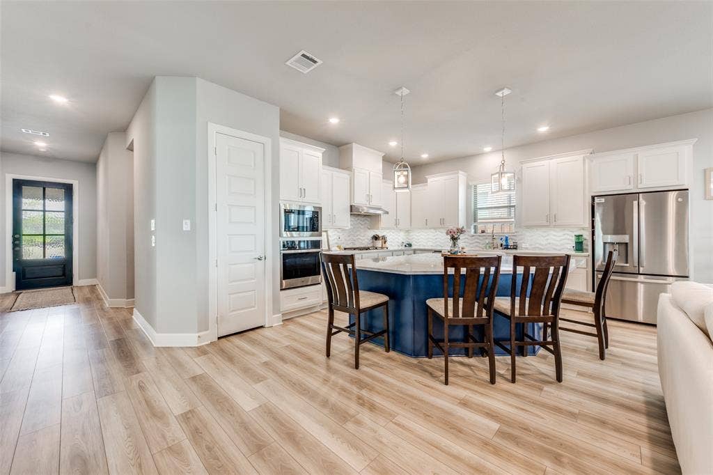 2703 Trinity Ridge Street, Mansfield, TX 76063 Open-concept kitchen featuring a blue island with a light countertop, white cabinetry, stainless steel appliances, and light wood-finish flooring