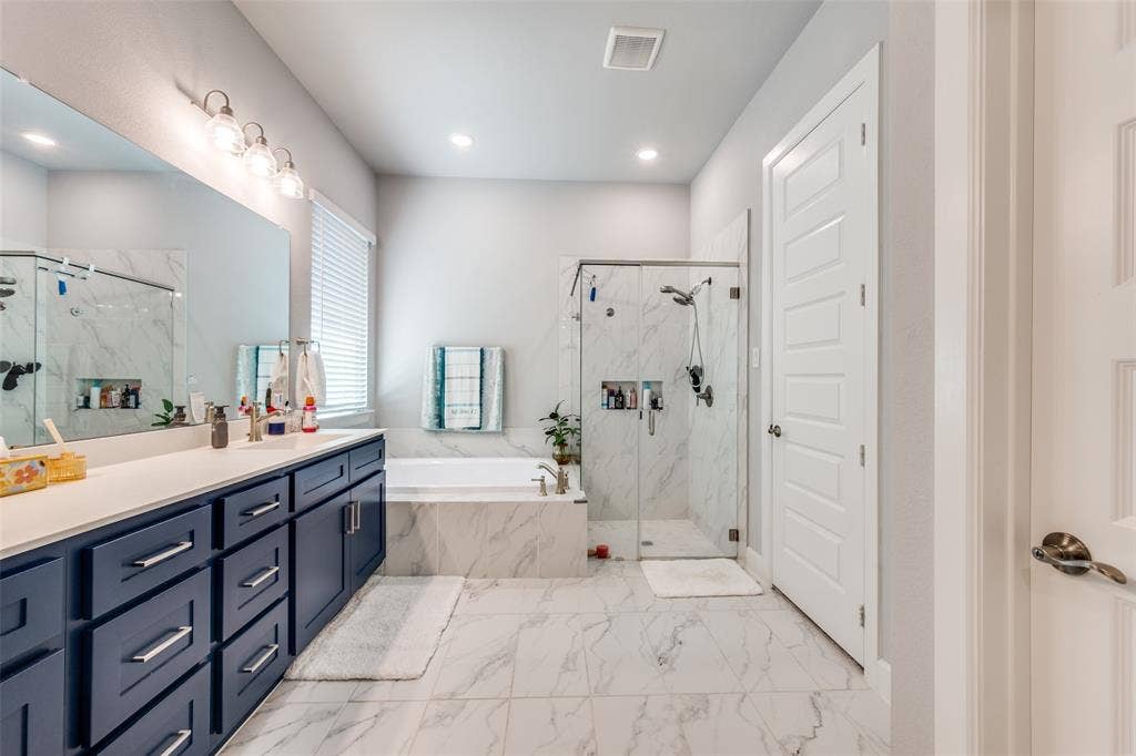 2703 Trinity Ridge Street, Mansfield, TX 76063 Spacious bathroom featuring a dual vanity with navy cabinetry and white countertops, a large soaking tub, and a glass-enclosed shower with subway tile surround