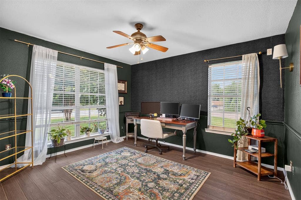 Spacious room featuring dark-toned walls with wainscoting, wood-finish flooring, and a ceiling fan with integrated lighting