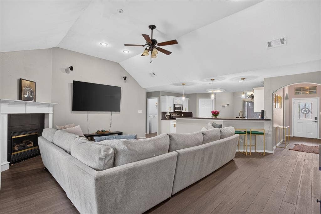 Spacious living area featuring wood-finish flooring, a white mantel fireplace, and a vaulted ceiling with a ceiling fan