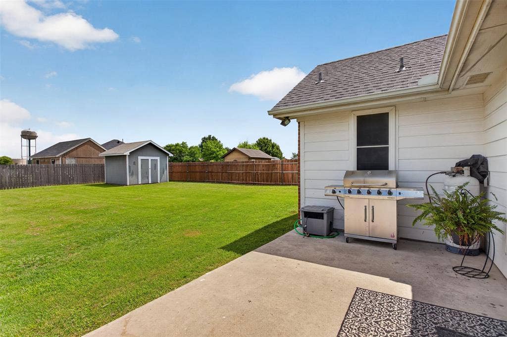 Expansive backyard featuring a large concrete patio, wood privacy fencing, and a separate storage shed