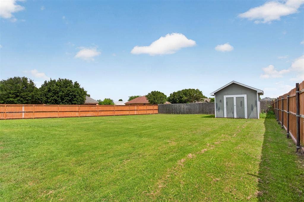 Expansive green lawn featuring a privacy fence, a detached storage shed, and mature perimeter trees