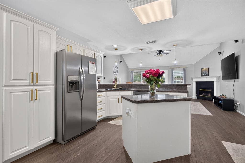 Kitchen with white cabinetry, stainless steel refrigerator, dark countertops, and wood-finish flooring