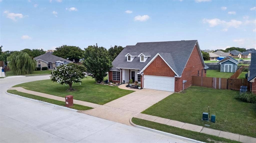 Brick exterior residence featuring a front-facing garage, dormer windows, and mature landscaping