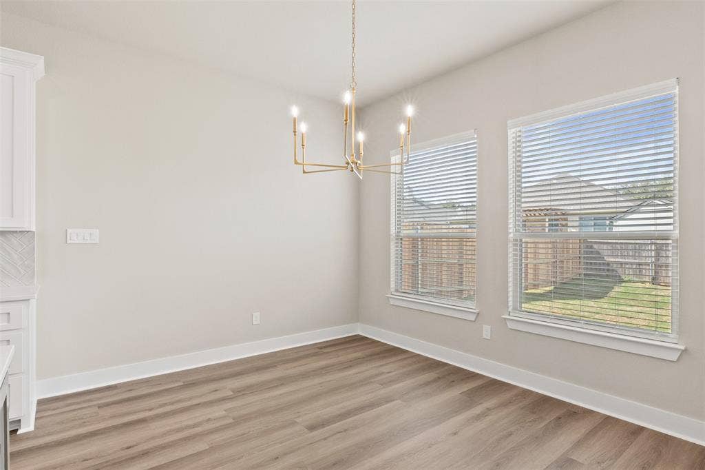 9824 Durango Trail, Waco, TX 76712 Dining area featuring wood-finish flooring, a modern gold-tone chandelier, two windows with blinds, and light-toned walls