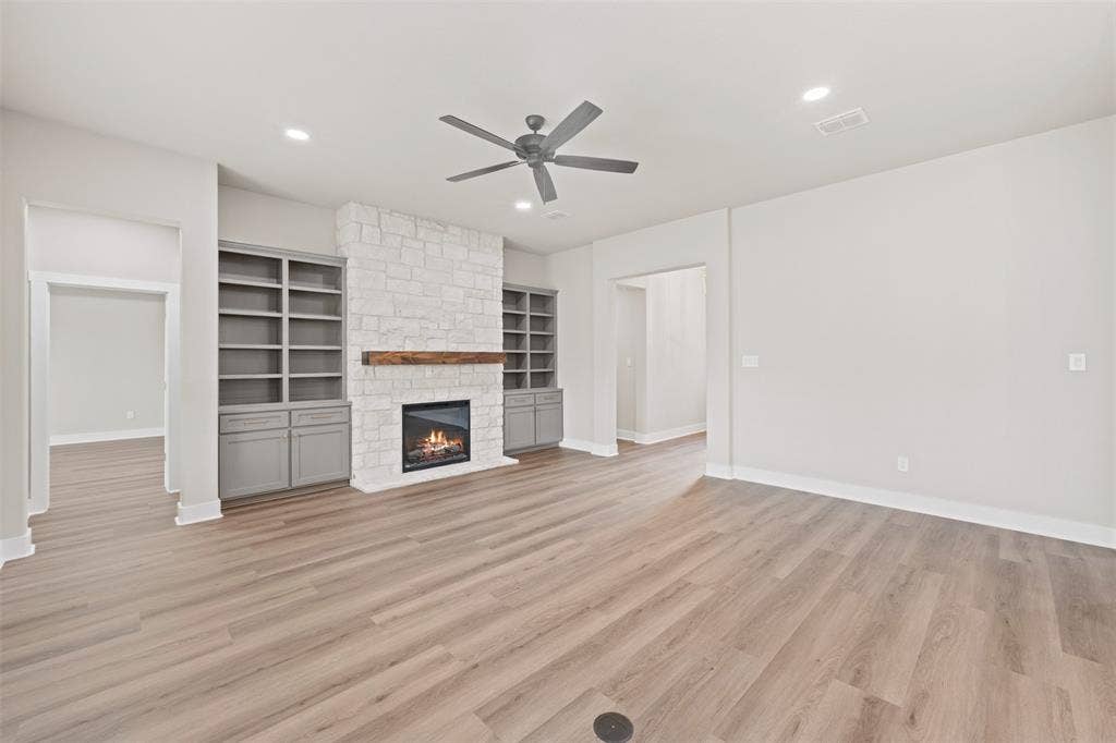 9824 Durango Trail, Waco, TX 76712 Spacious room featuring wood-finish flooring, a stone-clad fireplace with a wood mantel, and built-in shelving with lower cabinetry
