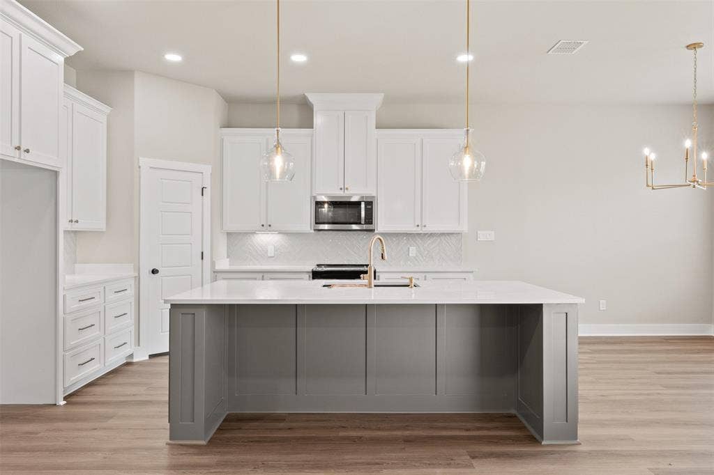 9824 Durango Trail, Waco, TX 76712 Modern kitchen featuring a spacious gray island with a white countertop, white cabinetry, brass pendant lighting, and wood-finish flooring