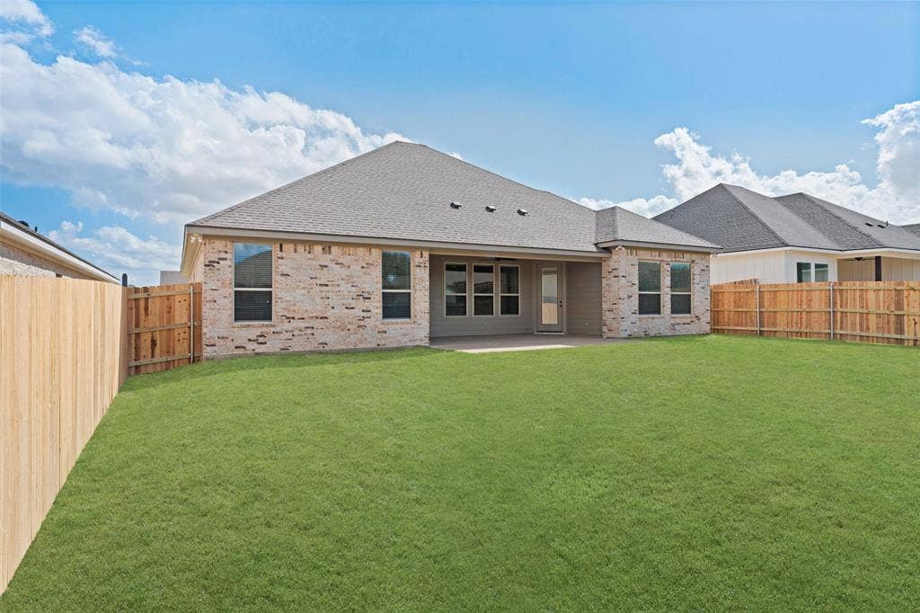 9824 Durango Trail, Waco, TX 76712 Expansive rear lawn featuring a privacy fence, brick exterior, multiple windows, and a covered patio area
