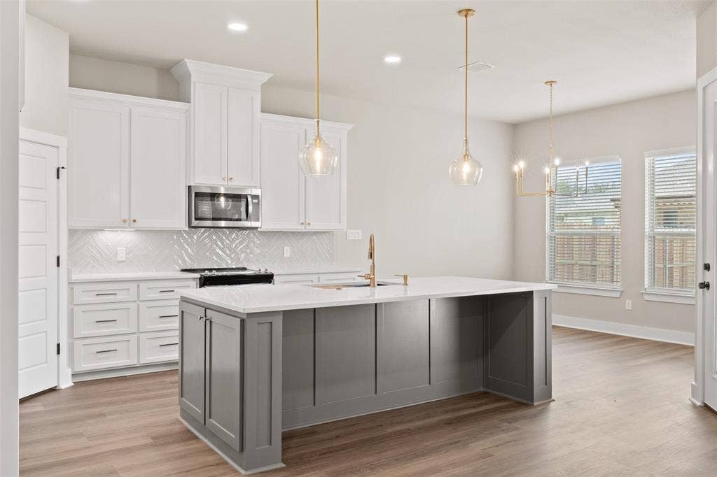 9824 Durango Trail, Waco, TX 76712 Modern kitchen featuring a large central island with a light-colored countertop, white shaker-style cabinetry, and wood-finish flooring