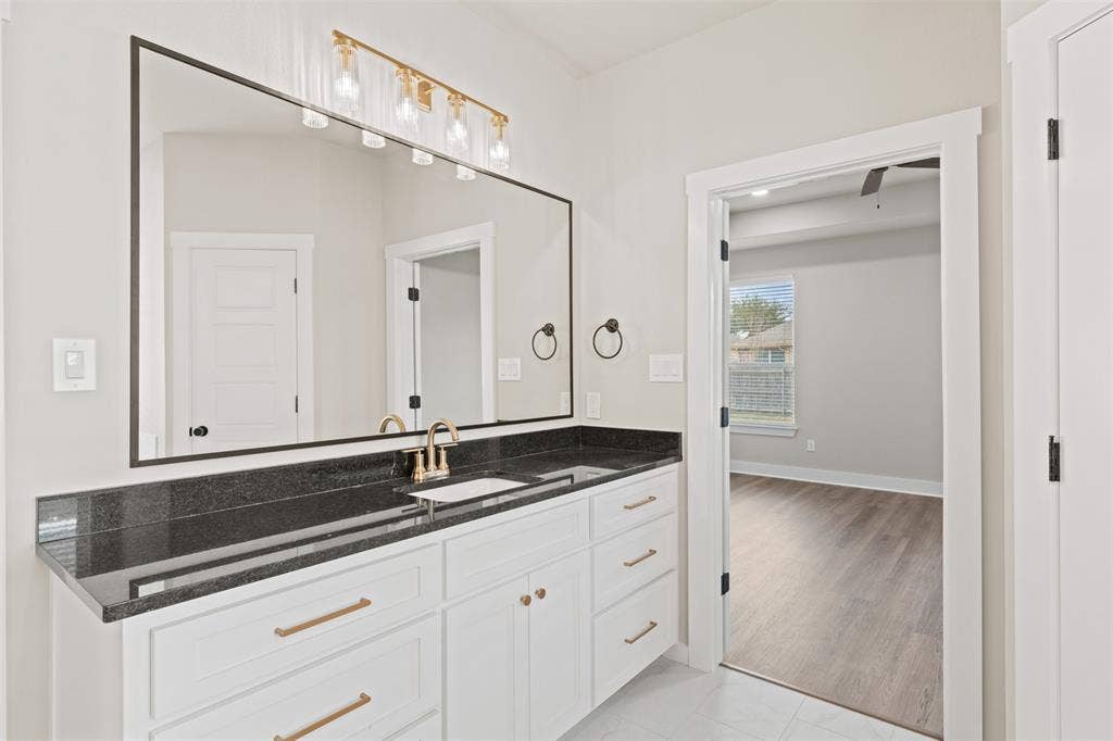 9824 Durango Trail, Waco, TX 76712 Bathroom vanity featuring a large mirror with a black frame, a dark stone countertop, and a white cabinet with gold-toned hardware