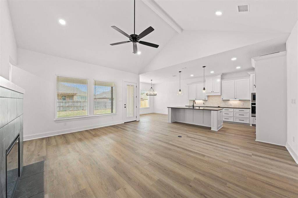 9820 Durango Trail, Waco, TX 76712 Open-concept living space featuring vaulted ceilings, wood-finish flooring, a modern fireplace, recessed lighting, and a kitchen with white cabinetry and a central island
