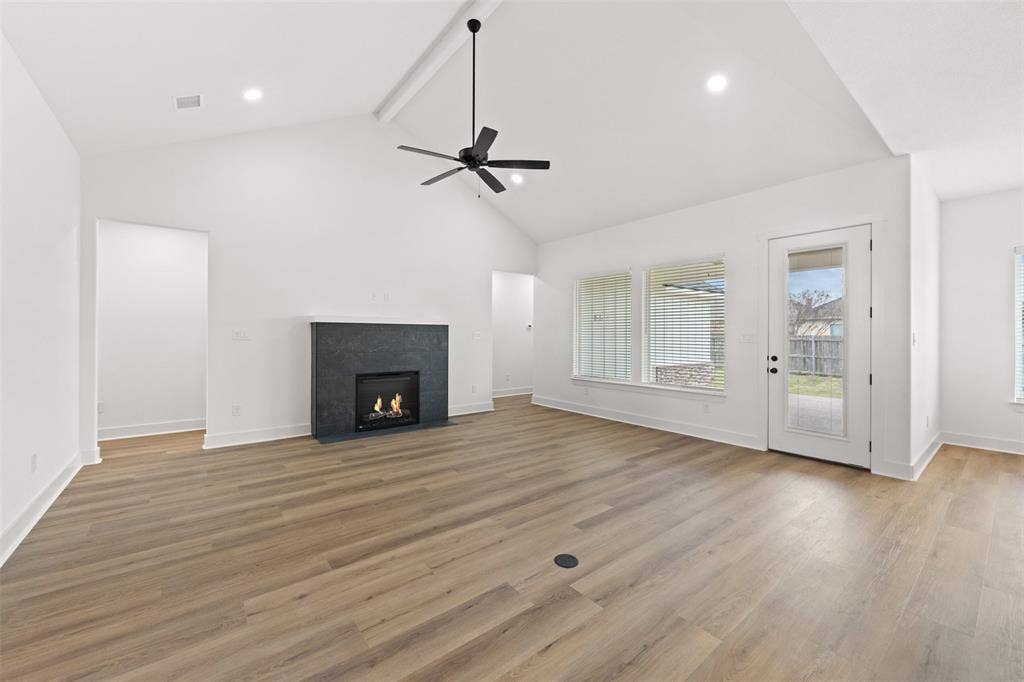 9820 Durango Trail, Waco, TX 76712 Spacious living area featuring vaulted ceilings, wood-finish flooring, a contemporary fireplace with a dark stone surround, a ceiling fan with integrated lighting, and a glass-paned exterior door