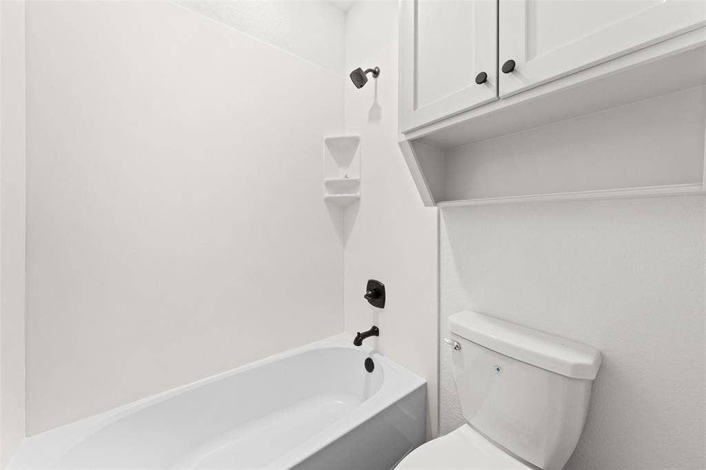 9820 Durango Trail, Waco, TX 76712 White bathtub with black fixtures, integrated corner shelving, and an overhead showerhead