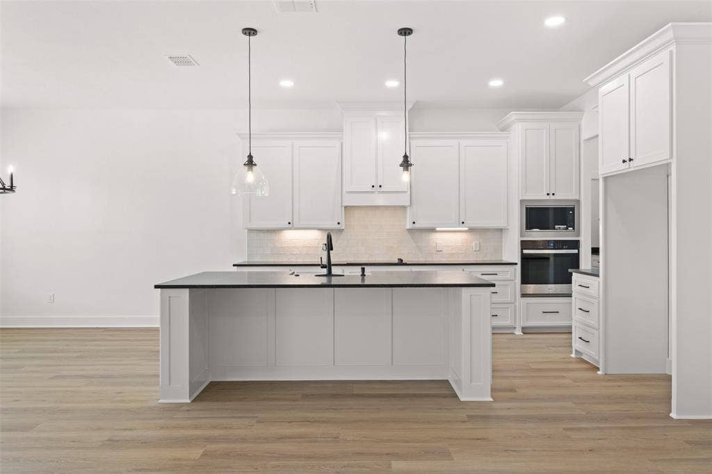 9820 Durango Trail, Waco, TX 76712 Bright kitchen featuring a central island with a sink, white cabinetry, dark countertops, and integrated stainless steel appliances