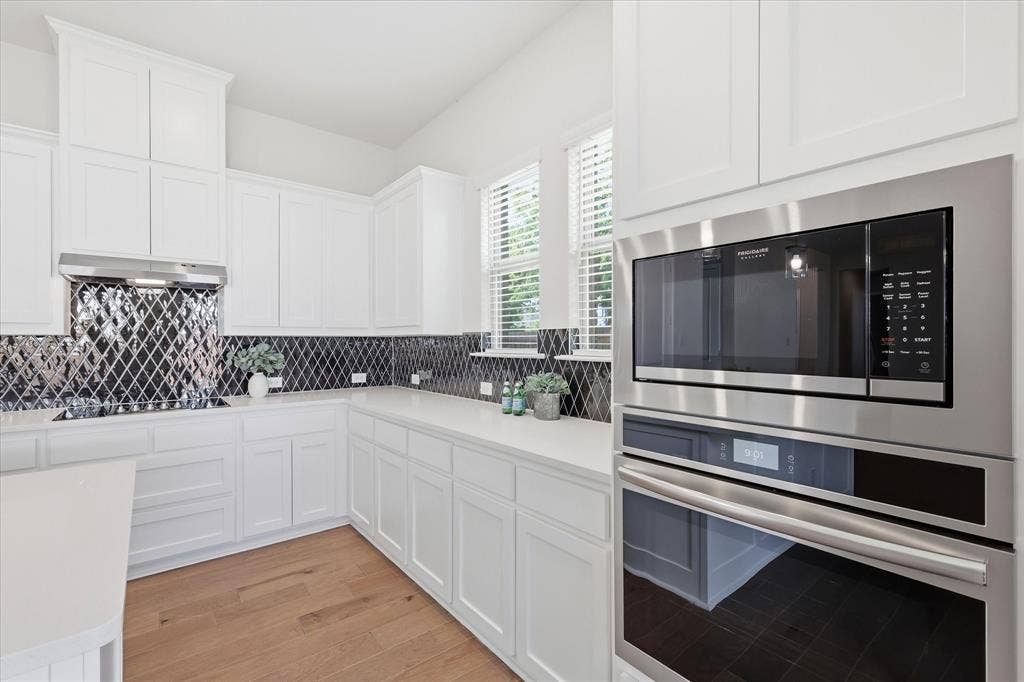 4017 Alpine Street, Midlothian, TX 76065 Contemporary kitchen featuring white cabinetry, light countertops, wood-finish flooring, a diamond-patterned backsplash, and stainless steel built-in appliances