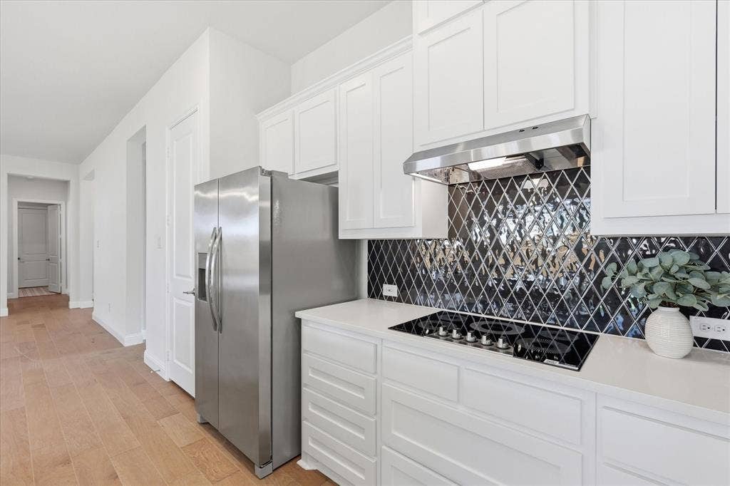 4017 Alpine Street, Midlothian, TX 76065 Kitchen featuring white cabinetry, a black diamond-patterned backsplash, a stainless steel range hood, an integrated cooktop, and light wood-finish flooring