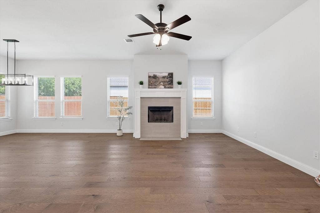 4017 Alpine Street, Midlothian, TX 76065 Spacious living area featuring wood-finish flooring, a fireplace with a tile surround and mantel, multiple windows with blinds, a ceiling fan, and a linear chandelier