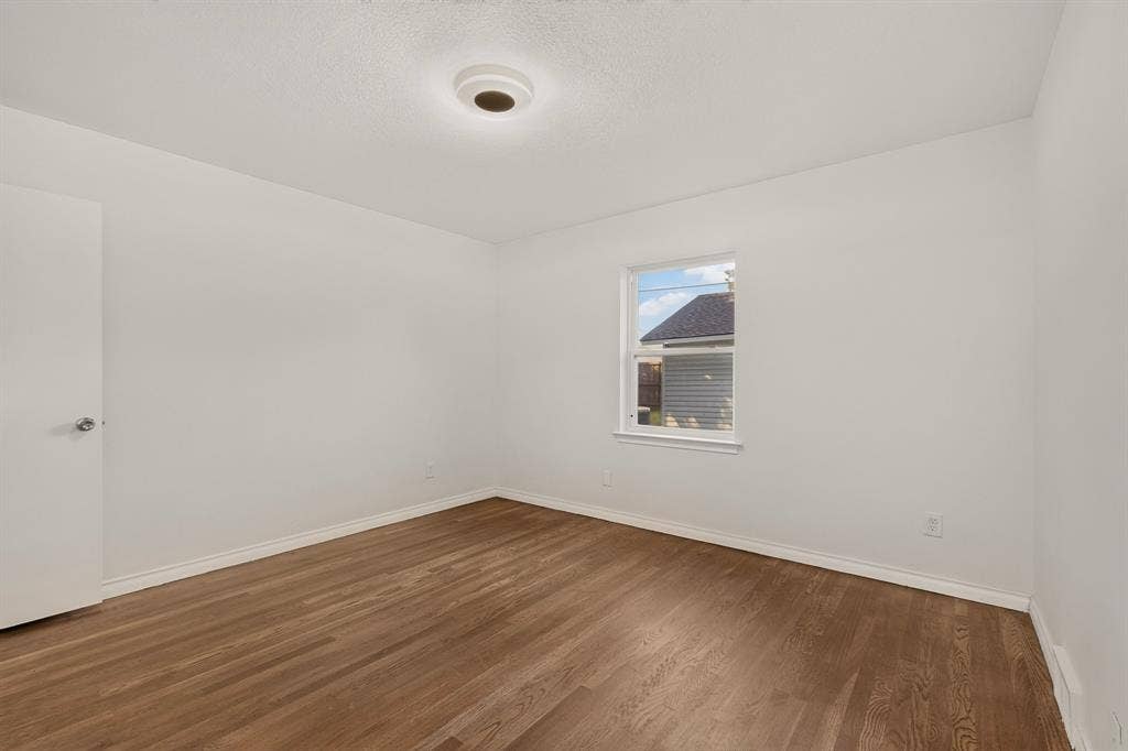 405 Easton Road, Dallas, TX 75218 Spacious room featuring wood-finish flooring, white baseboards, and a single window with white trim
