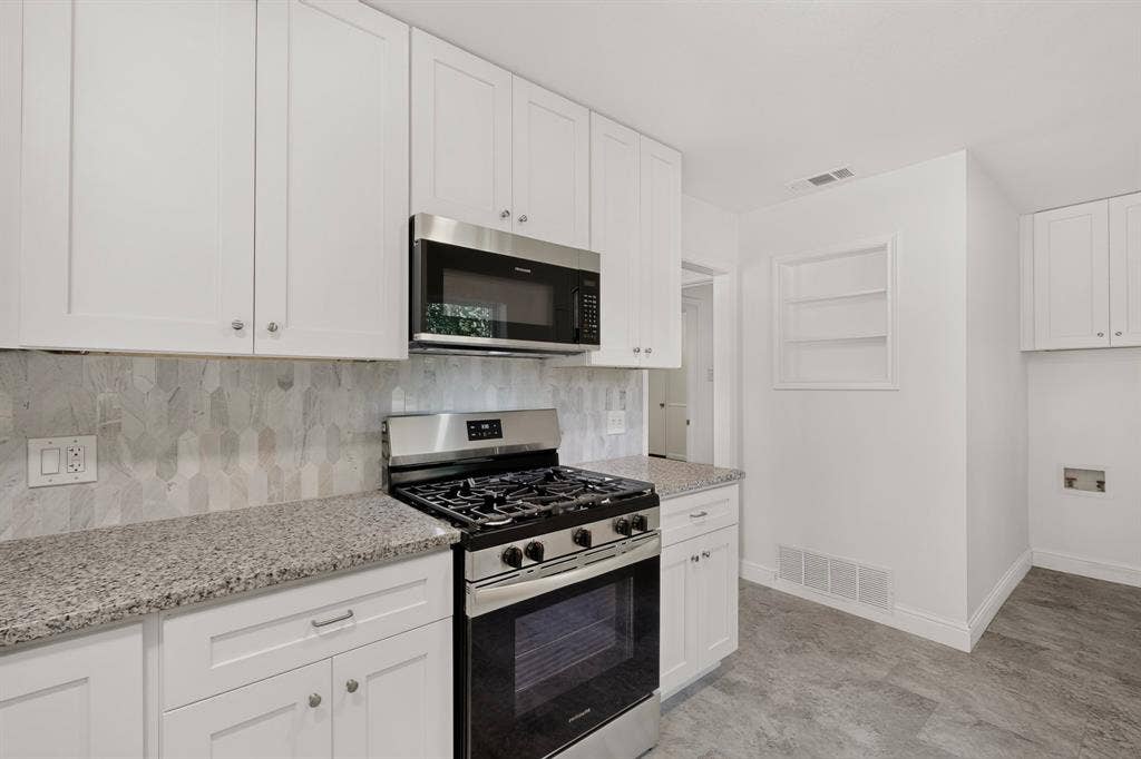 405 Easton Road, Dallas, TX 75218 Modern kitchen featuring stainless steel appliances, white cabinetry, granite countertops, a patterned tile backsplash, and wood-finish flooring