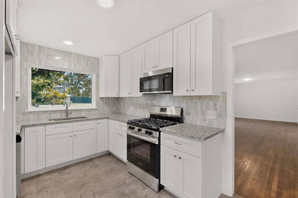 405 Easton Road, Dallas, TX 75218 Corner kitchen featuring white shaker cabinetry, stainless steel appliances, speckled stone countertops, and a full-height tile backsplash