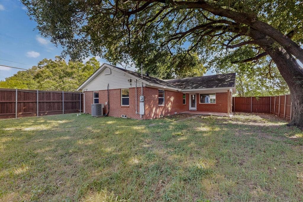 405 Easton Road, Dallas, TX 75218 Expansive backyard featuring a red brick exterior, a mature tree providing shade, a wood privacy fence, and a concrete patio