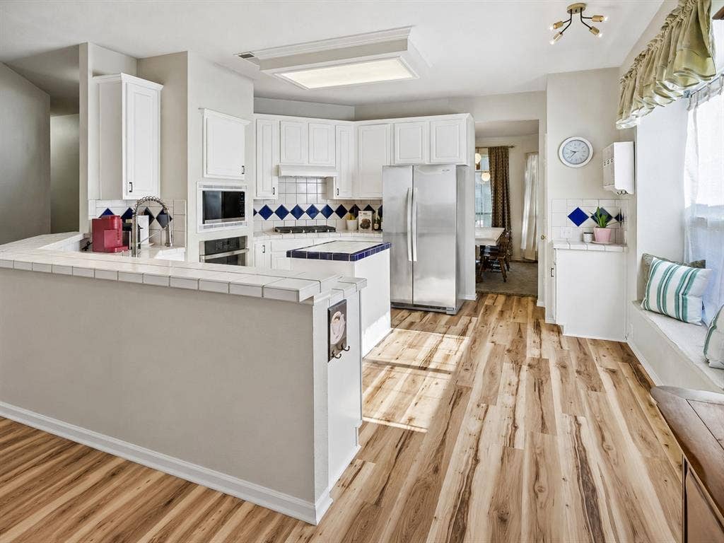 11379 Lockshire Drive, Frisco, TX 75035 Wood-finish flooring, white cabinetry, tile countertops, stainless steel refrigerator, and a built-in window seat