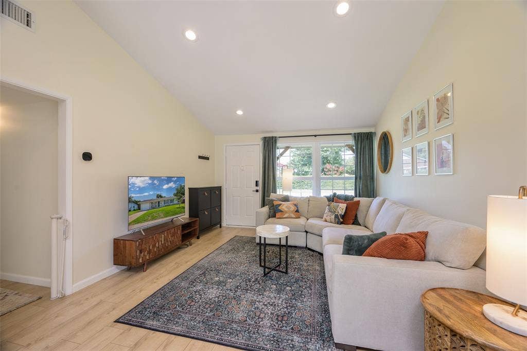 Living area featuring wood-finish flooring, vaulted ceilings, recessed lighting, and a large window with exterior views