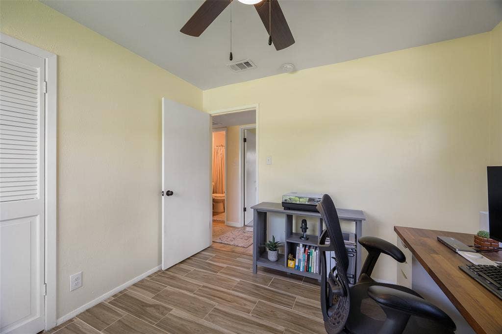 Room featuring wood-look tile flooring, light-toned walls, a white door with a black knob, a louvered bi-fold door, and a ceiling fan with light fixture