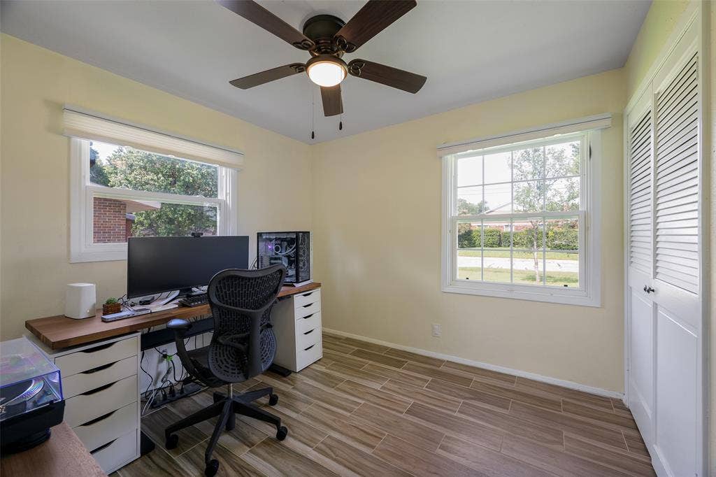 Room featuring wood-finish tile flooring, two white-framed windows, and a ceiling fan with integrated lighting