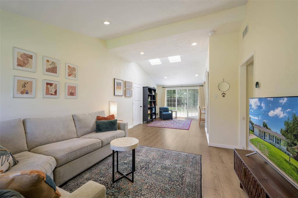 Spacious living area featuring vaulted ceilings with recessed lighting, skylights, wood-finish flooring, and sliding glass doors