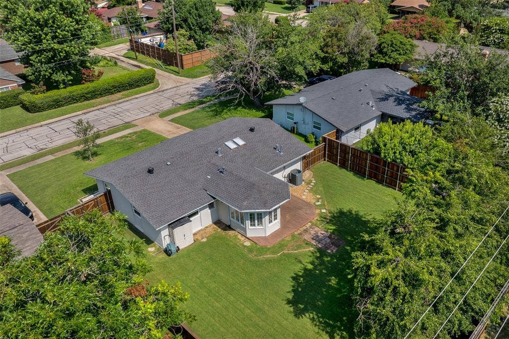 Aerial view of a single-story residence with a dark shingle roof featuring multiple skylights