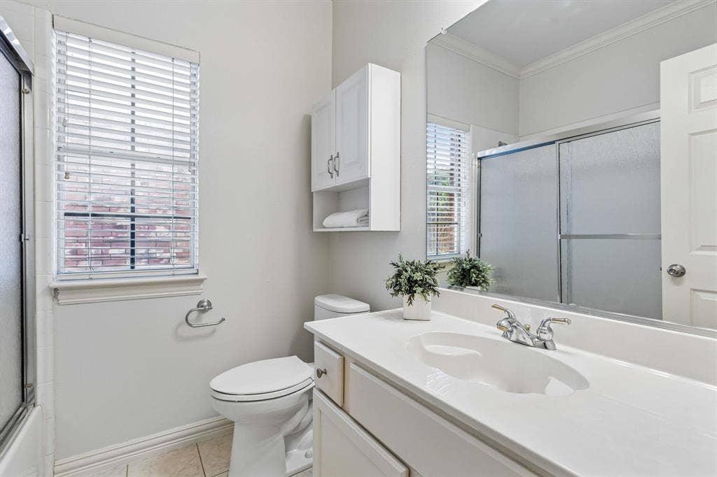 6852 High Field Trail, Plano, TX 75023 Bathroom featuring a white vanity with integrated sink, a large wall-mounted mirror, and a shower with sliding glass doors